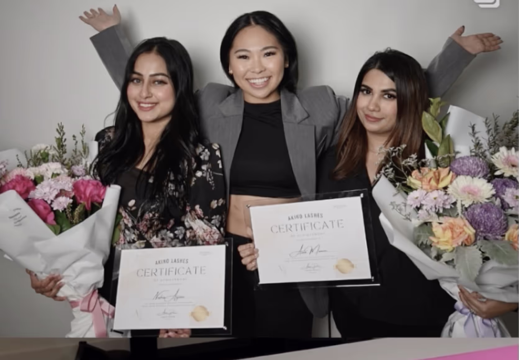 Lash trainer posing with graduates proudly displaying their eyelash extension course certificates.