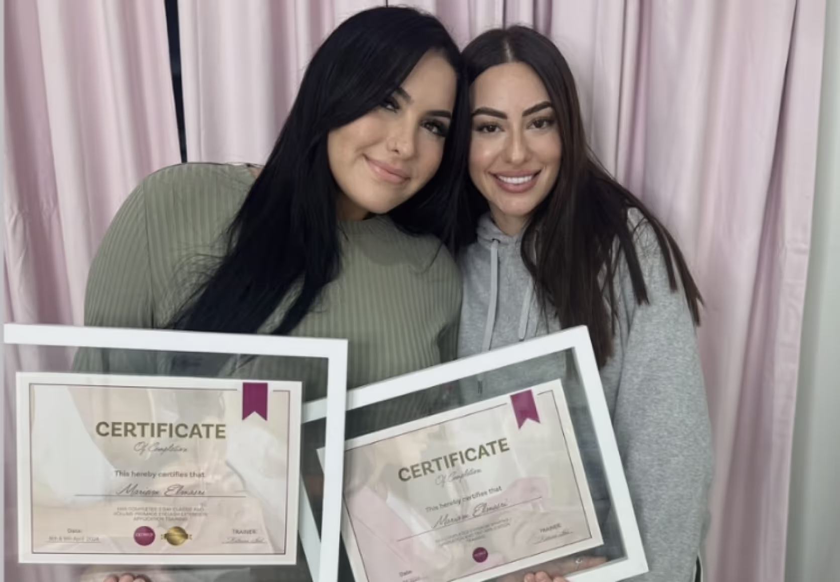 Trainer and student holding framed lash certification diplomas in beauty studio setting