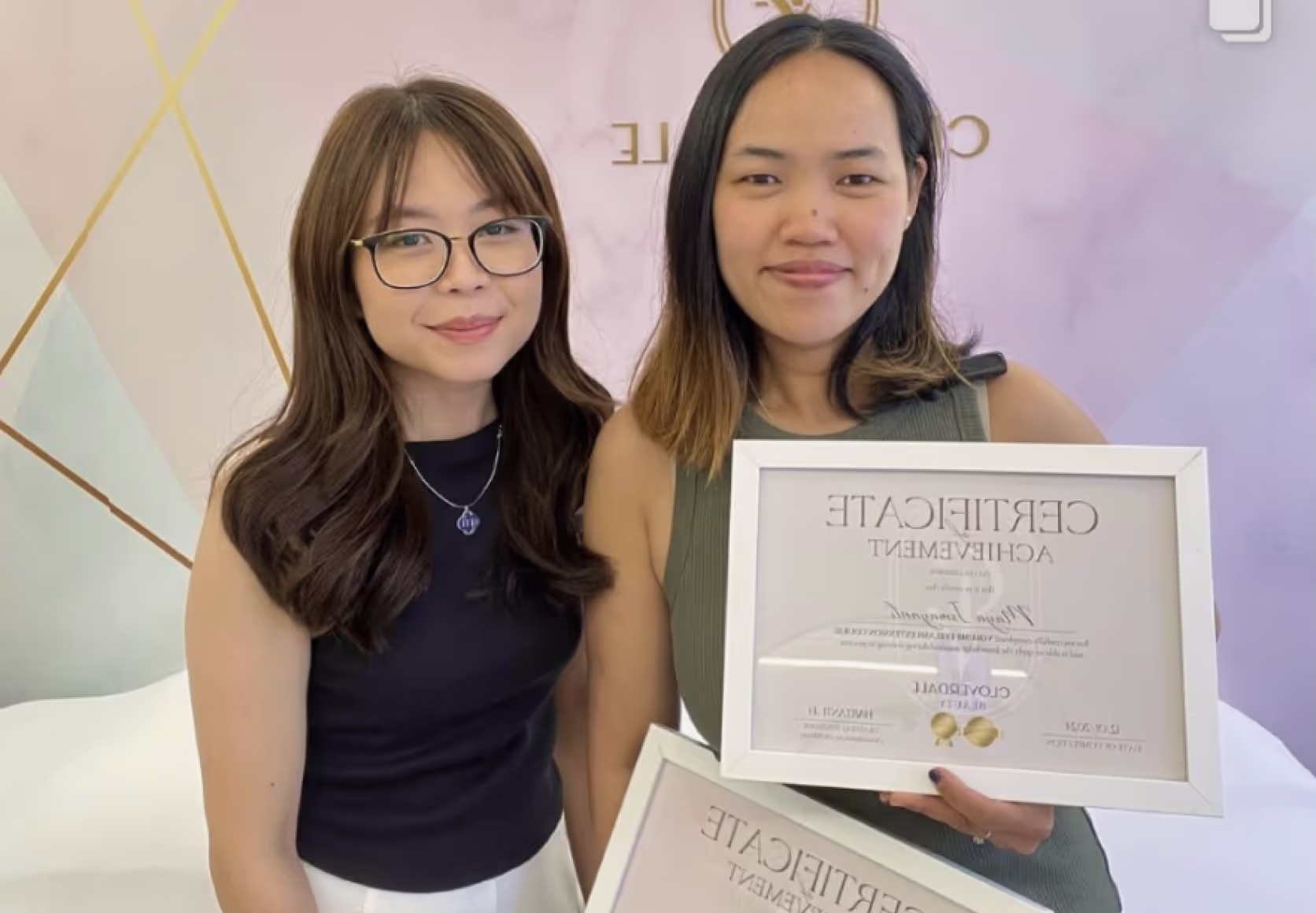 Trainer and student holding framed lash certification diploma in beauty studio setting.