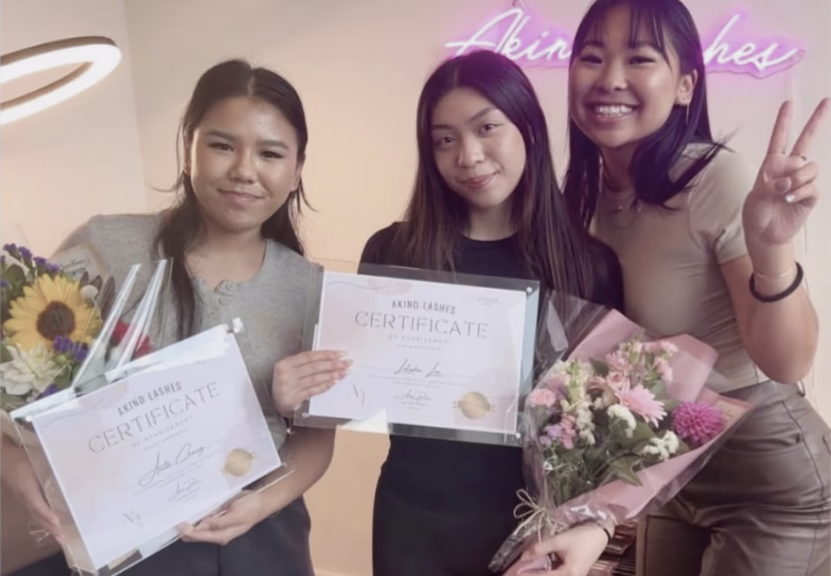 Trainer and students holding framed lash certification diplomas in beauty studio setting.
