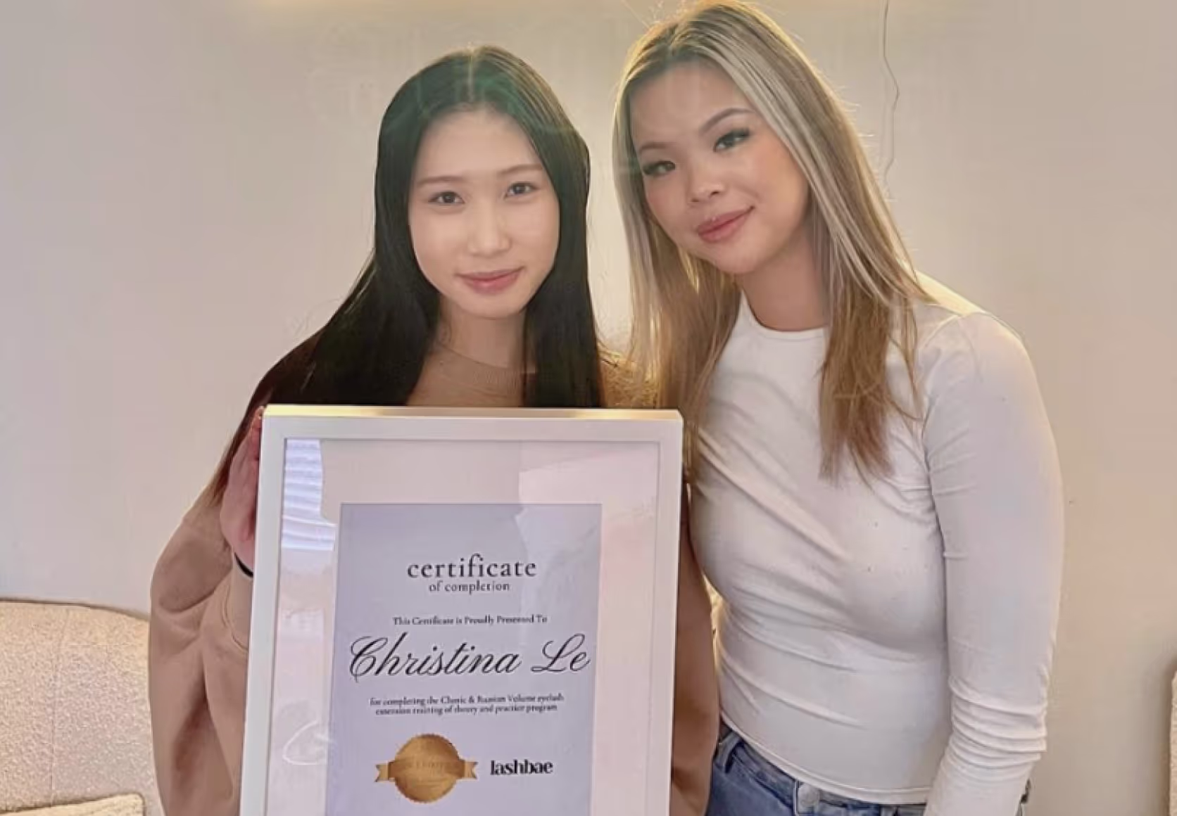 Trainer and students holding framed lash certification diplomas in beauty studio setting