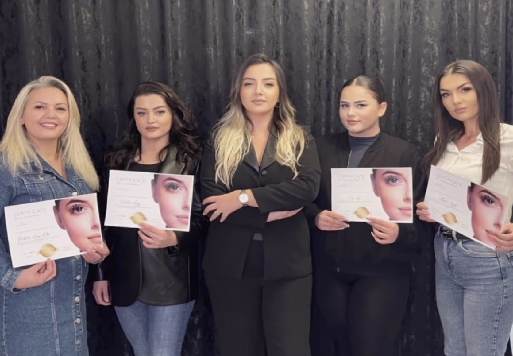 Lash trainer posing with graduates proudly displaying their eyelash extension course certificates.
