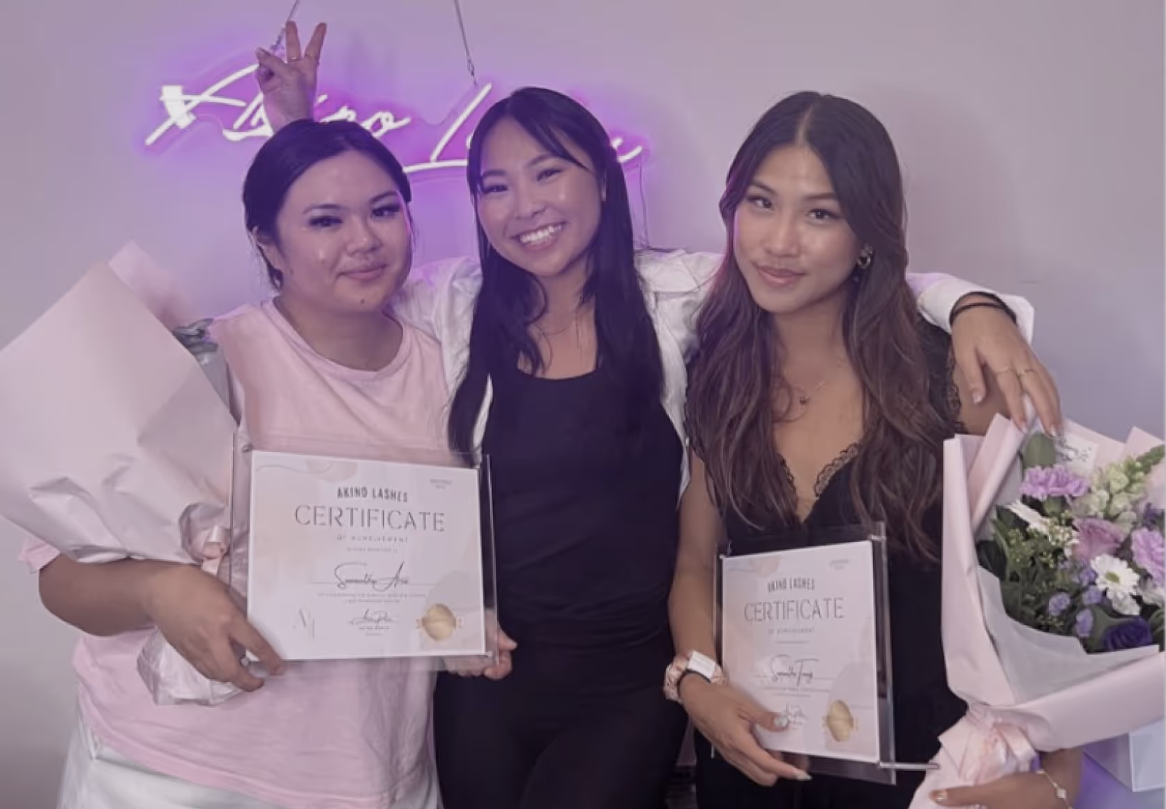 Lash trainer posing with graduates proudly displaying their eyelash extension course certificates.