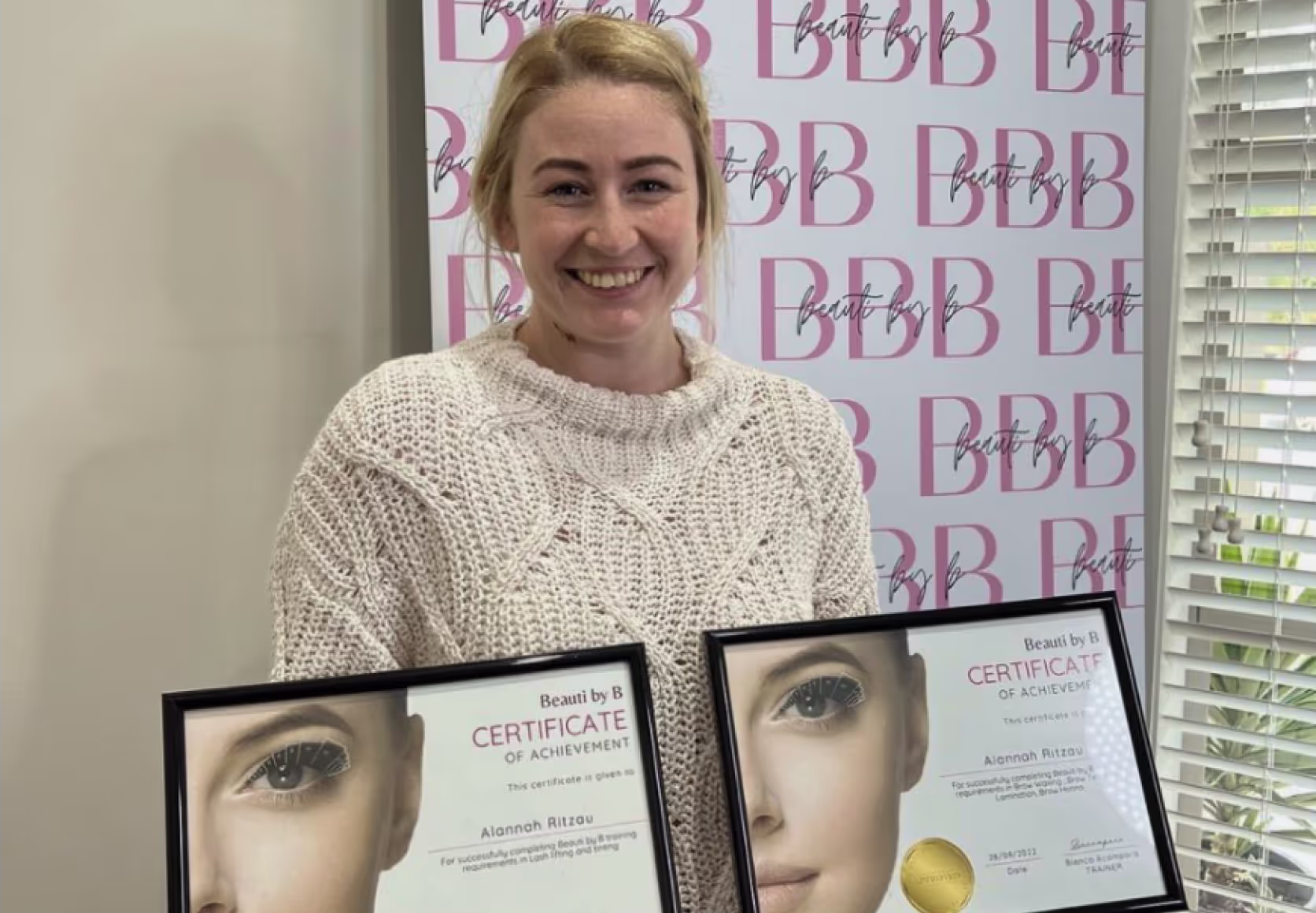Student holding framed lash certification diplomas in beauty studio setting.