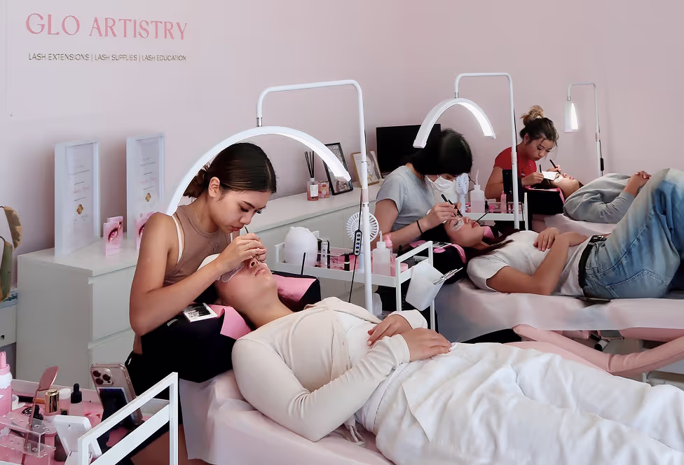 Lash artists at GLO Artistry performing eyelash extension treatments on clients in a professional training environment.