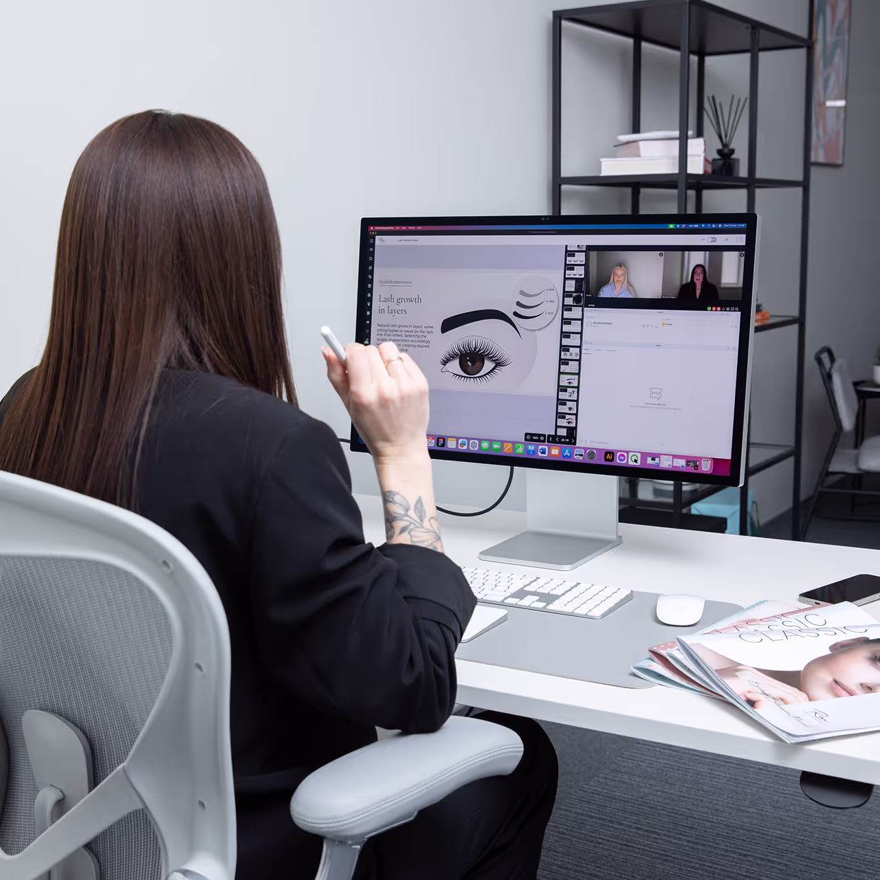 Lash educator teaching online lash extension course via video call, demonstrating eyelash growth theory on screen in a modern office setting.