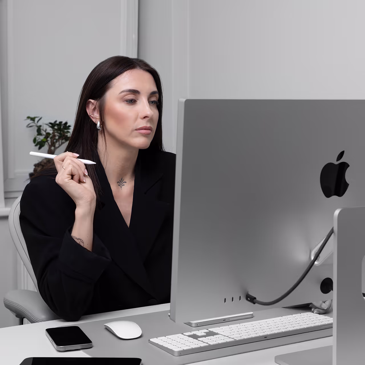 Lash educator sitting at a desk with an Apple computer, holding an Apple Pencil, representing RM Lash Academy’s online certification course.