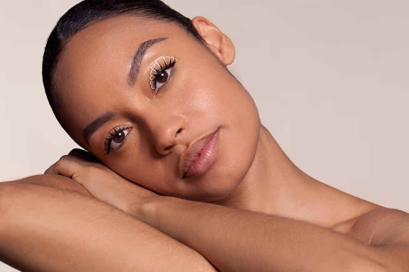 Close-up of a woman resting her head on her arms, featuring lash mapping illustration on eyelid and soft, natural makeup.